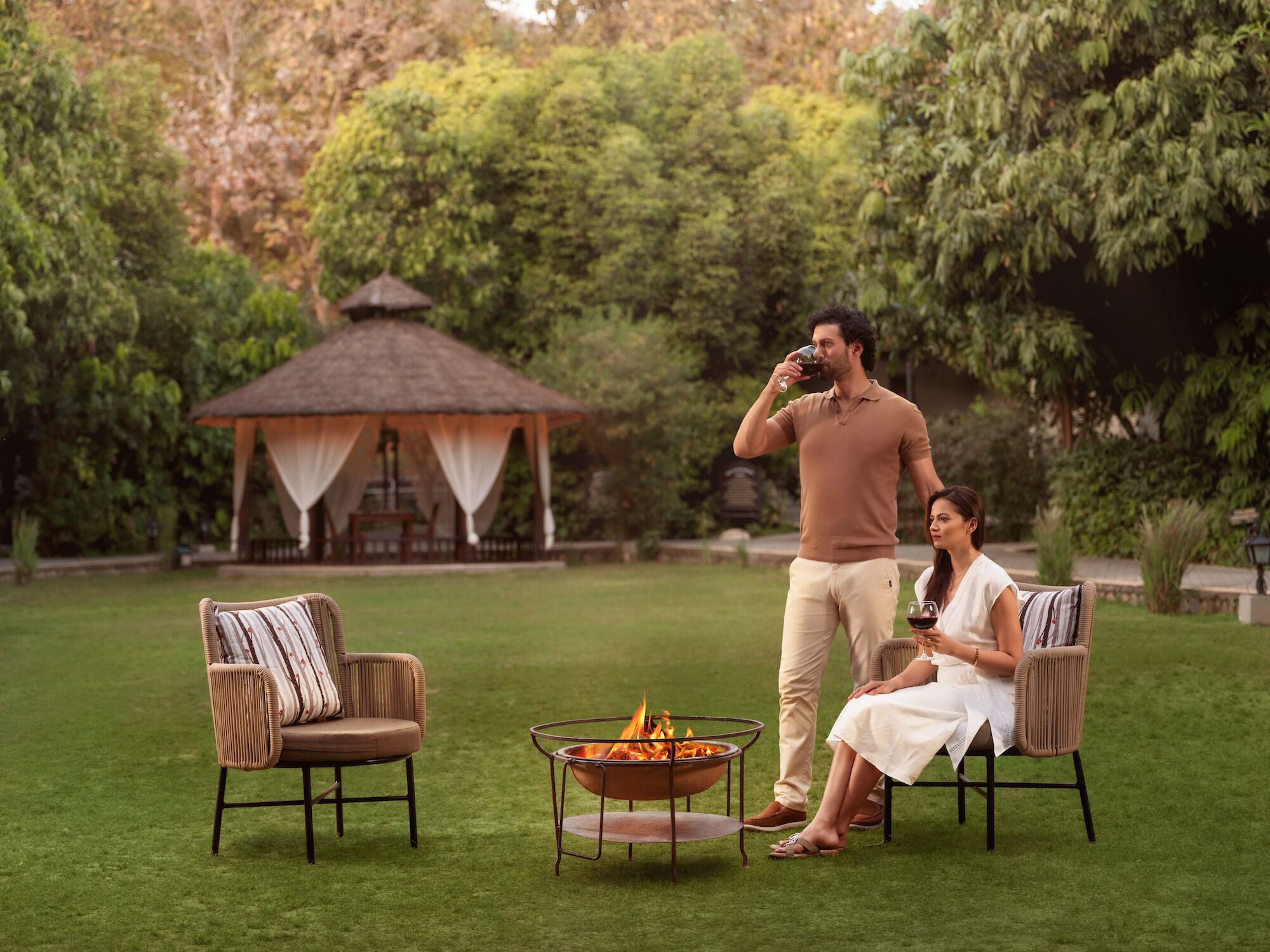 A couple sitting by a fire pit in a garden with a gazebo in the background.