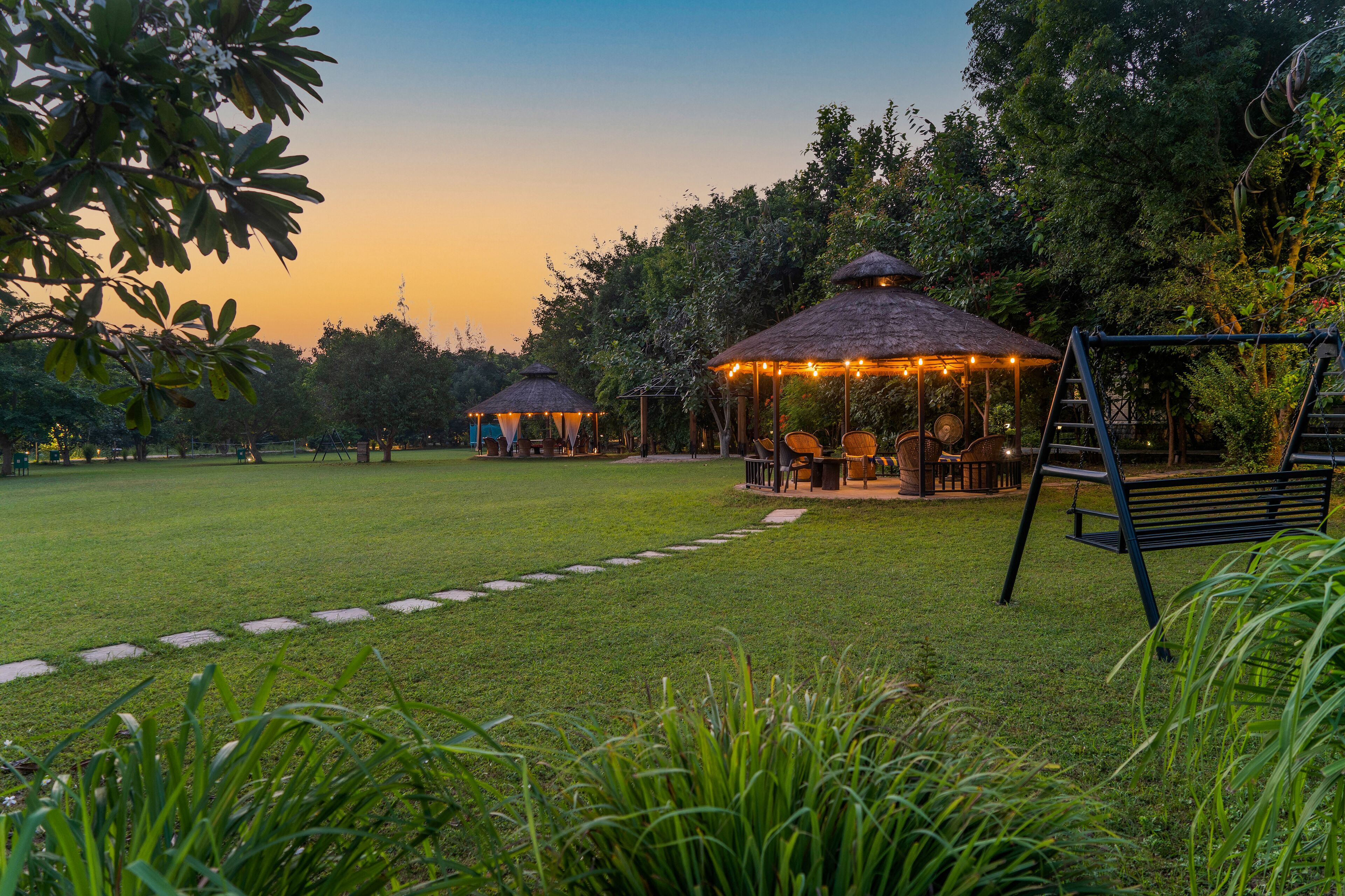 A well-maintained grassy area with thatched-roof gazebos, a swing set, and a paved walkway.