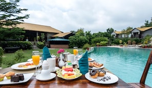A breakfast setup with a pool view, including plates with toast, muffins, and fruit, and a table with a teapot and cups. - Aahana Resort & Spa - Jim Corbett (Ramnagar)