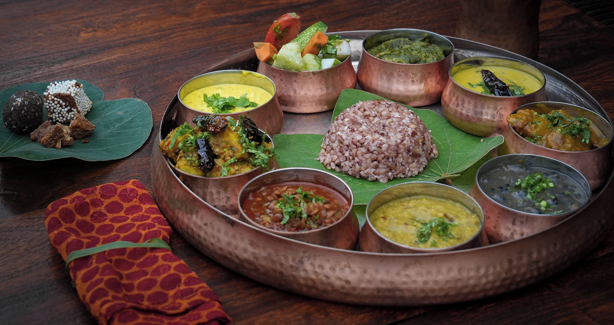 Comida tradicional india servida en una bandeja de cobre con diversos platos, incluyendo arroz, curris y una ensalada.