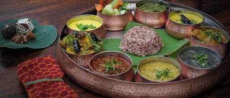 Comida tradicional india servida en una bandeja de cobre con diversos platos, incluyendo arroz, curris y una ensalada.