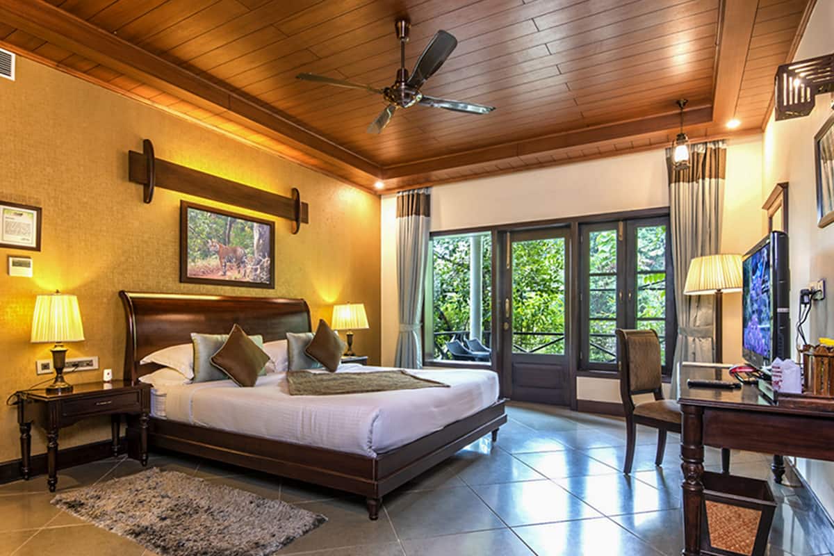 A spacious bedroom with a large bed, a desk, and a chair. There is a ceiling fan and a window with curtains.
