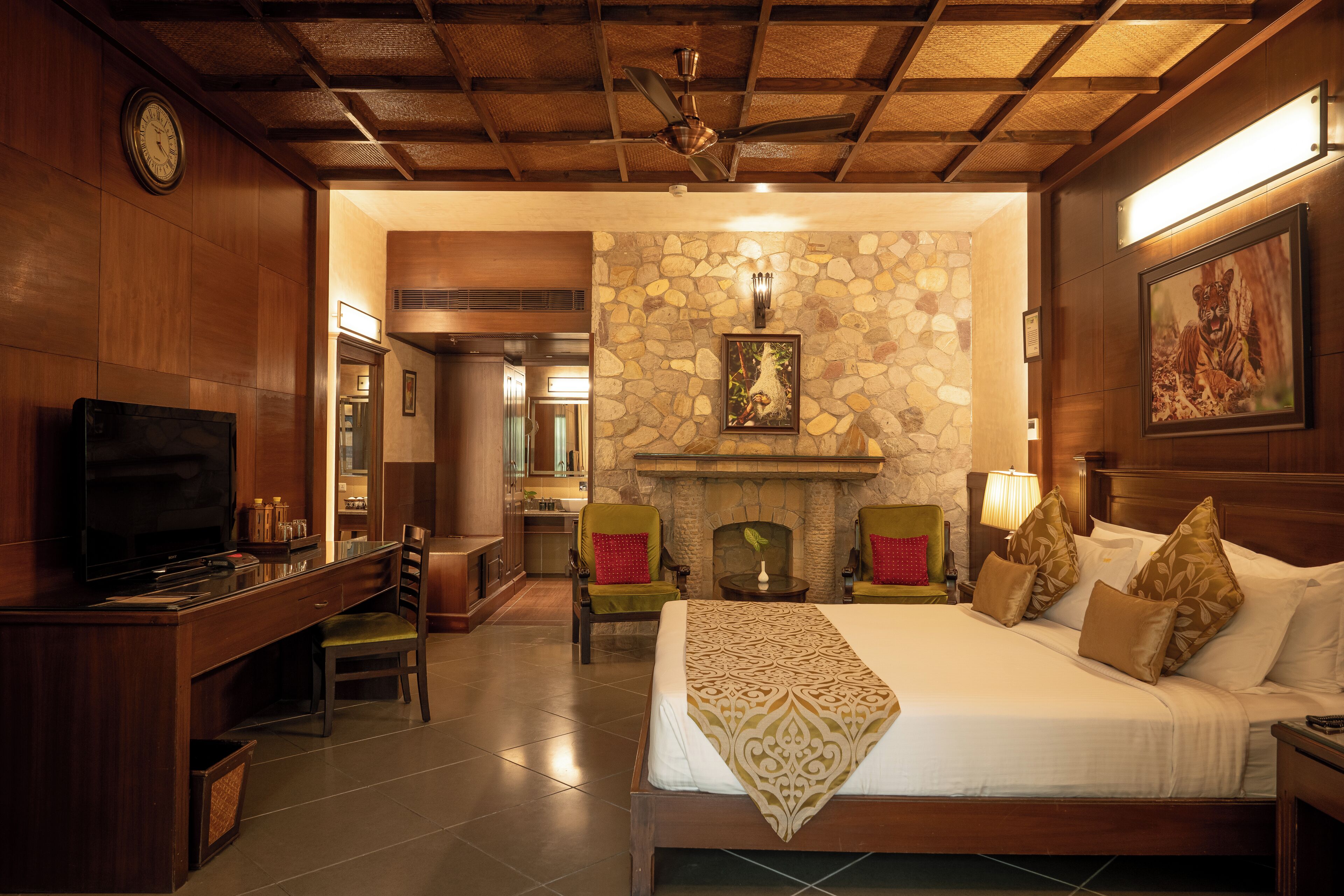 A hotel room with a bed, a desk with a TV, a fireplace, and a clock on the wall.