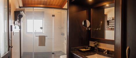 A modern bathroom with a wooden ceiling, a glass-enclosed shower, a sink with a mirror, and a toilet.
