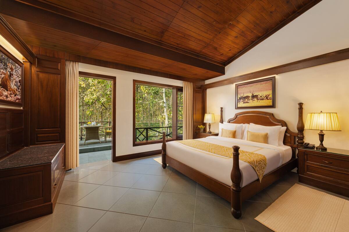 A spacious bedroom with a large bed, wooden ceiling, and a balcony with a view of greenery.