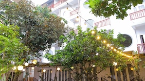 A courtyard with trees, string lights, and a white building with balconies. - Hoi An Paradise Hotel (Da Nang)