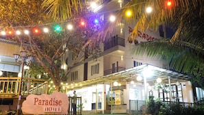 A hotel entrance with a sign reading "Paradise Hotel," surrounded by string lights and palm trees. - Hoi An Paradise Hotel (Da Nang)