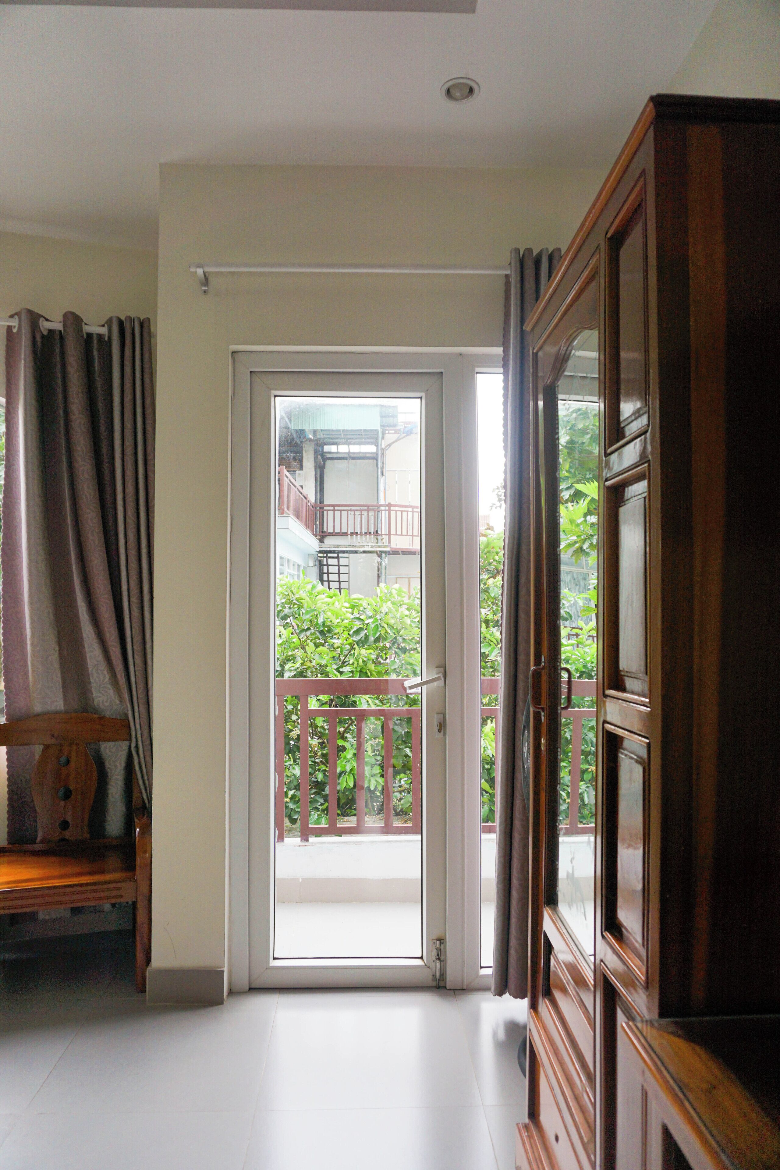 A room with a wooden cabinet, a bench, and a sliding glass door leading to a balcony with a red railing and greenery.