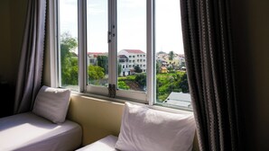A room with two beds, a window with curtains, and a view of buildings and greenery outside. - Hoi An Paradise Hotel (Da Nang)
