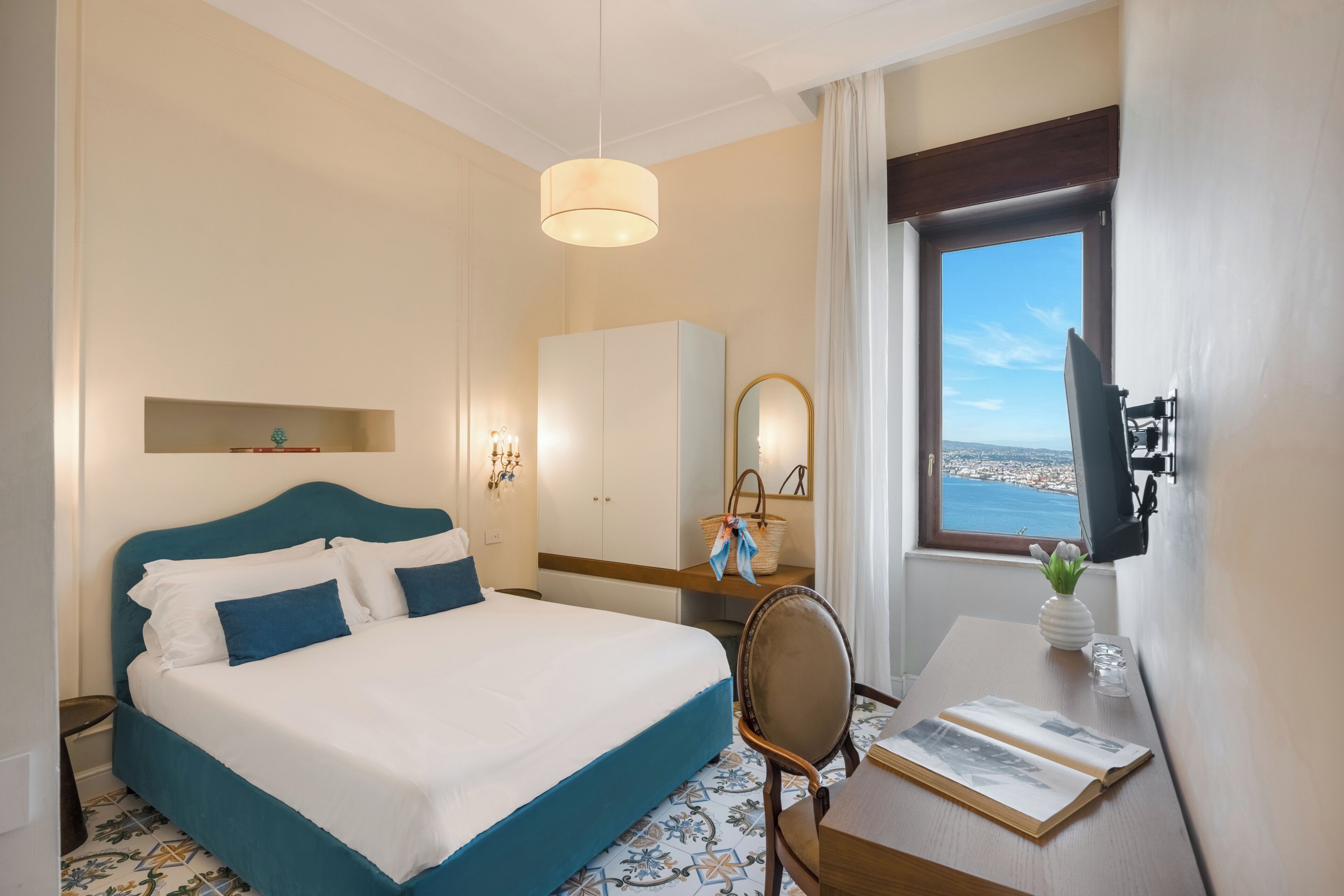 A hotel room with a bed, a desk, a chair, a television, a window with a view, and a wardrobe.