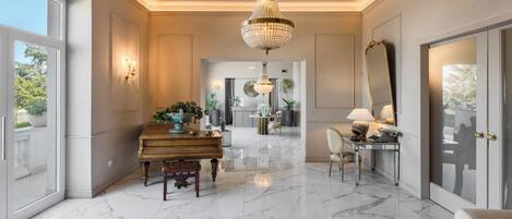 A spacious living room with a piano, a chandelier, and a large mirror.