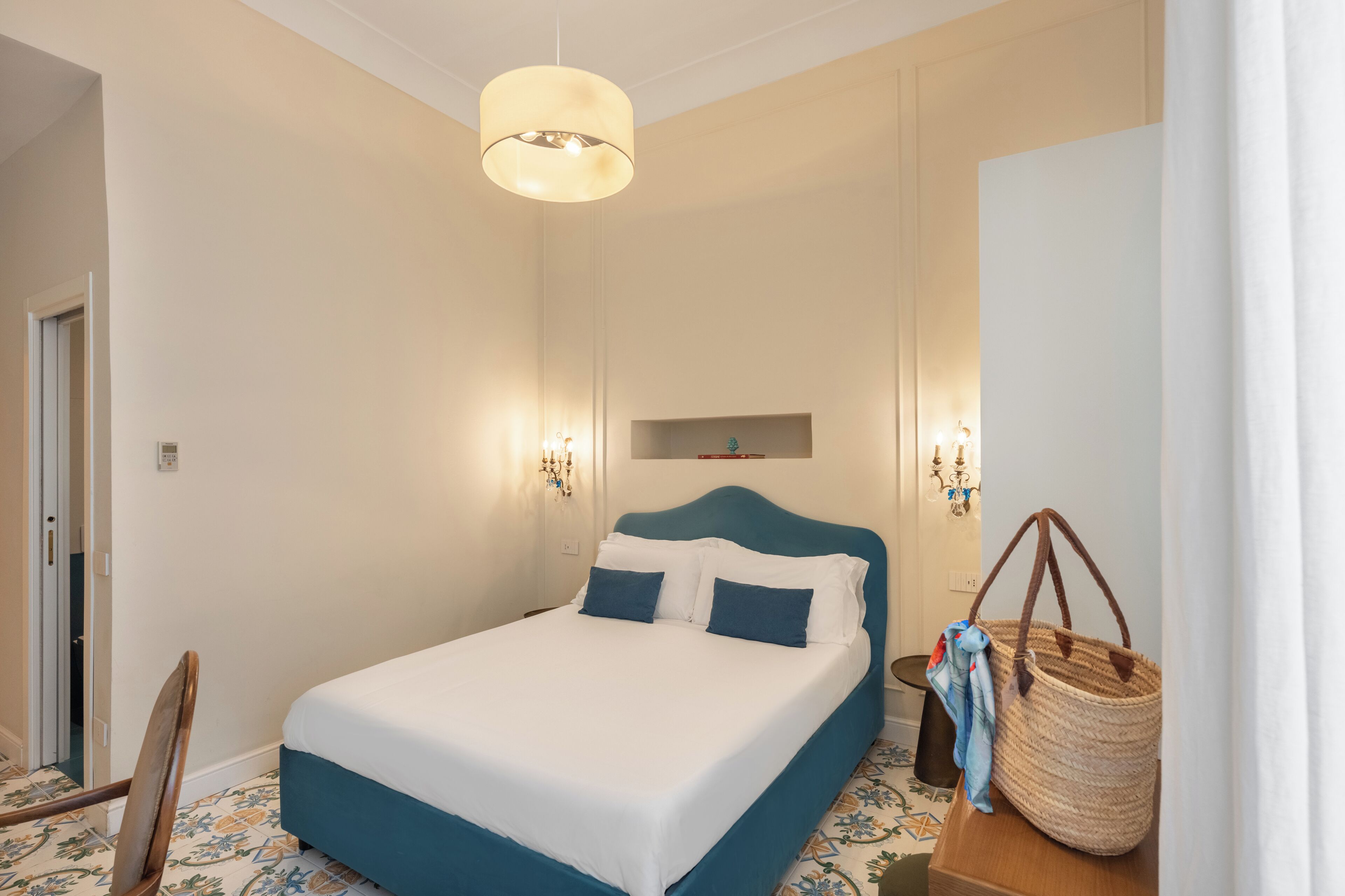 Un dormitorio con cama, lámpara colgante, mesita de noche y estante en la pared.