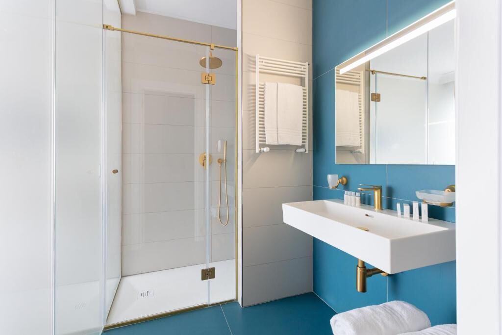 A modern bathroom with a glass shower enclosure, a white sink with gold fixtures, and a blue accent wall.