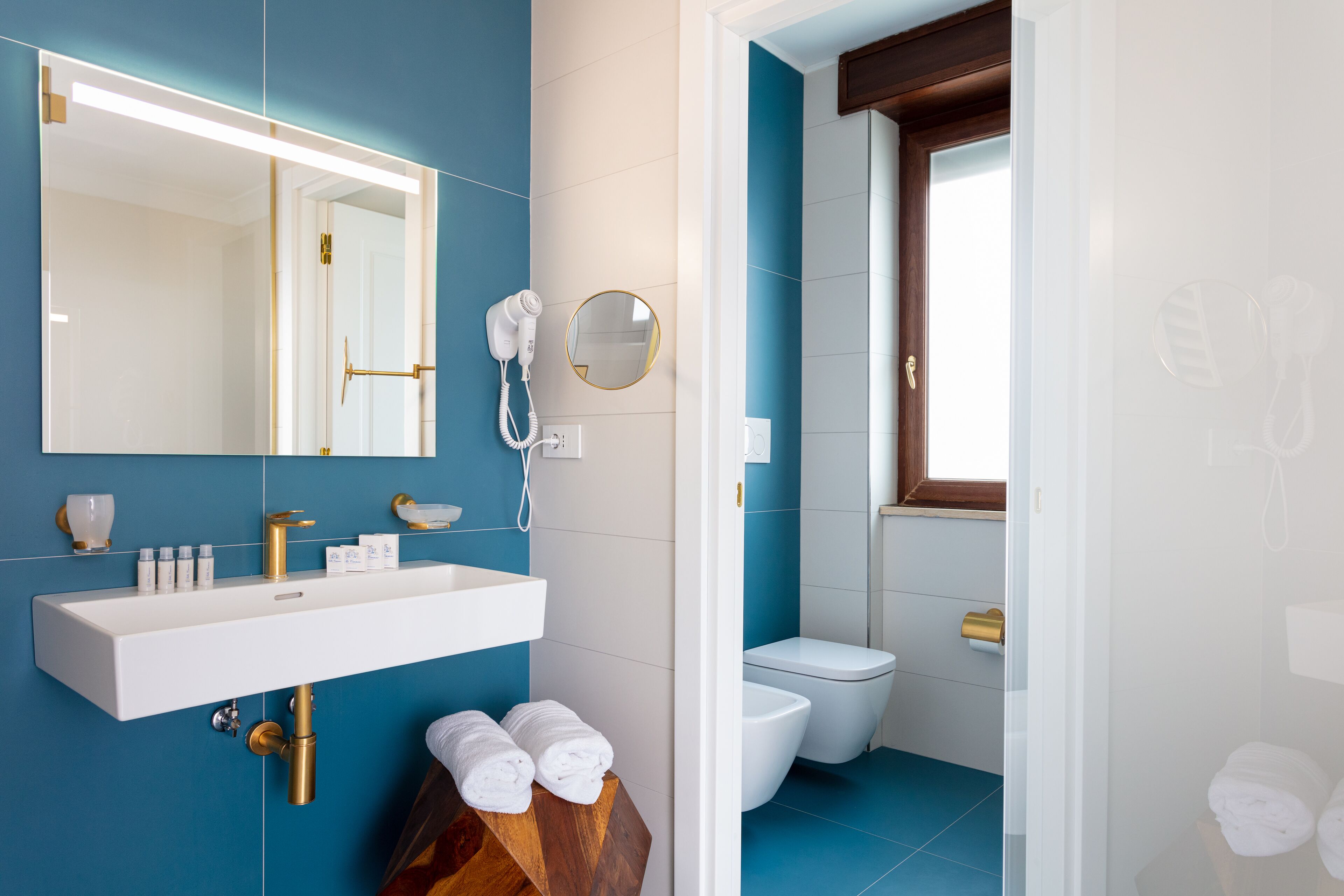 A modern bathroom with a white sink, gold fixtures, and a blue tiled wall.