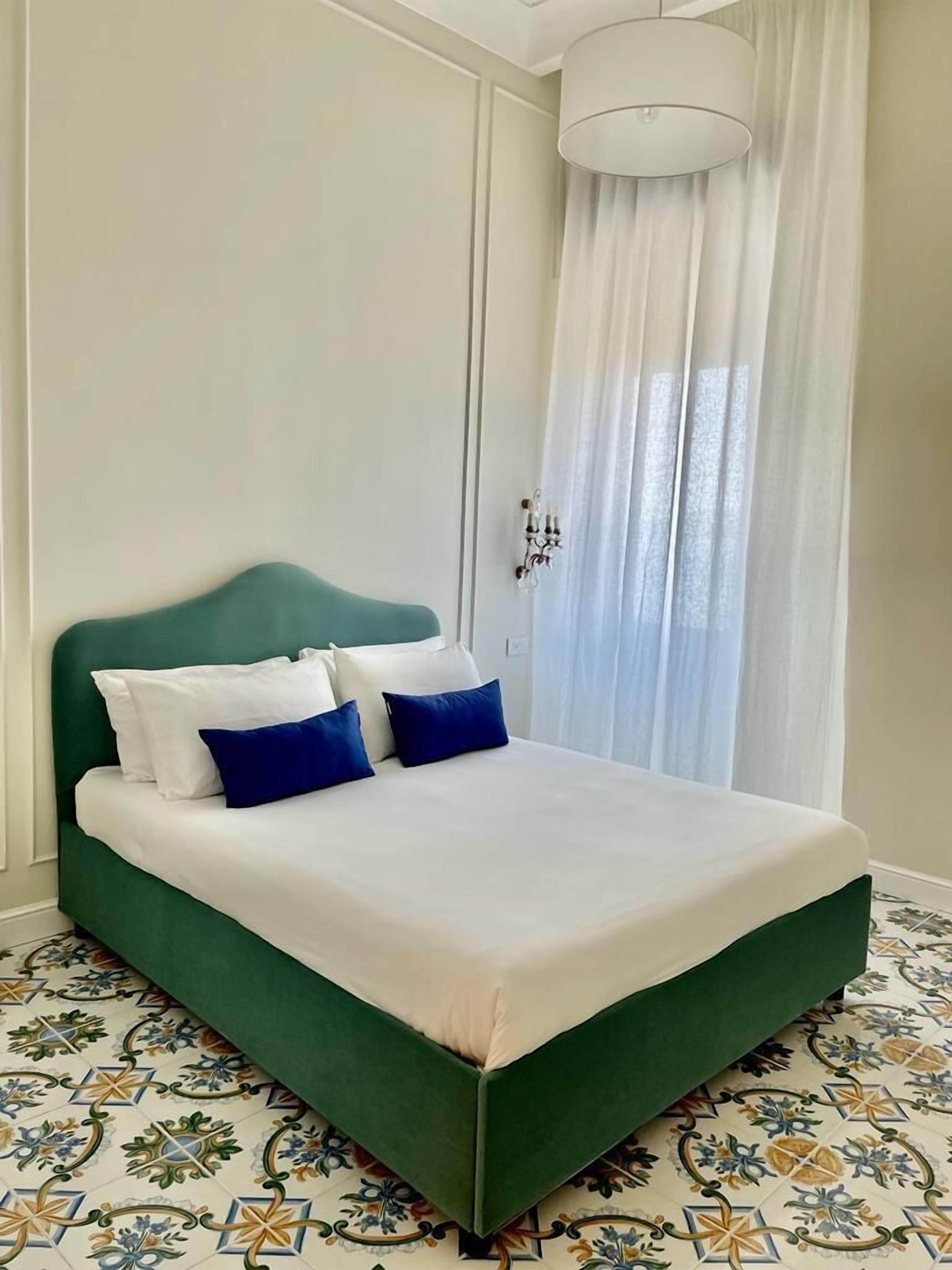 Una cama con cabecera verde, ropa de cama blanca y almohadas azules.