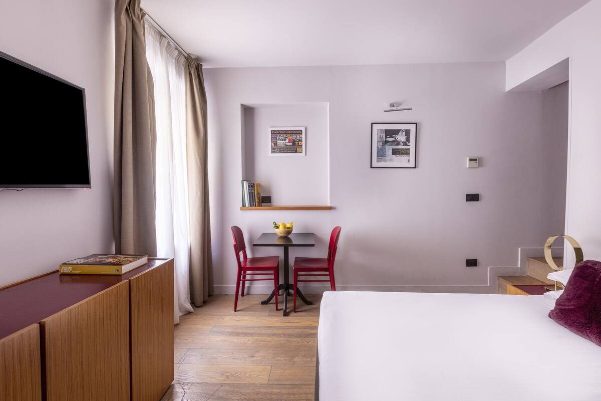 A hotel room with a bed, a desk, a TV, a dining table with chairs, and a staircase.