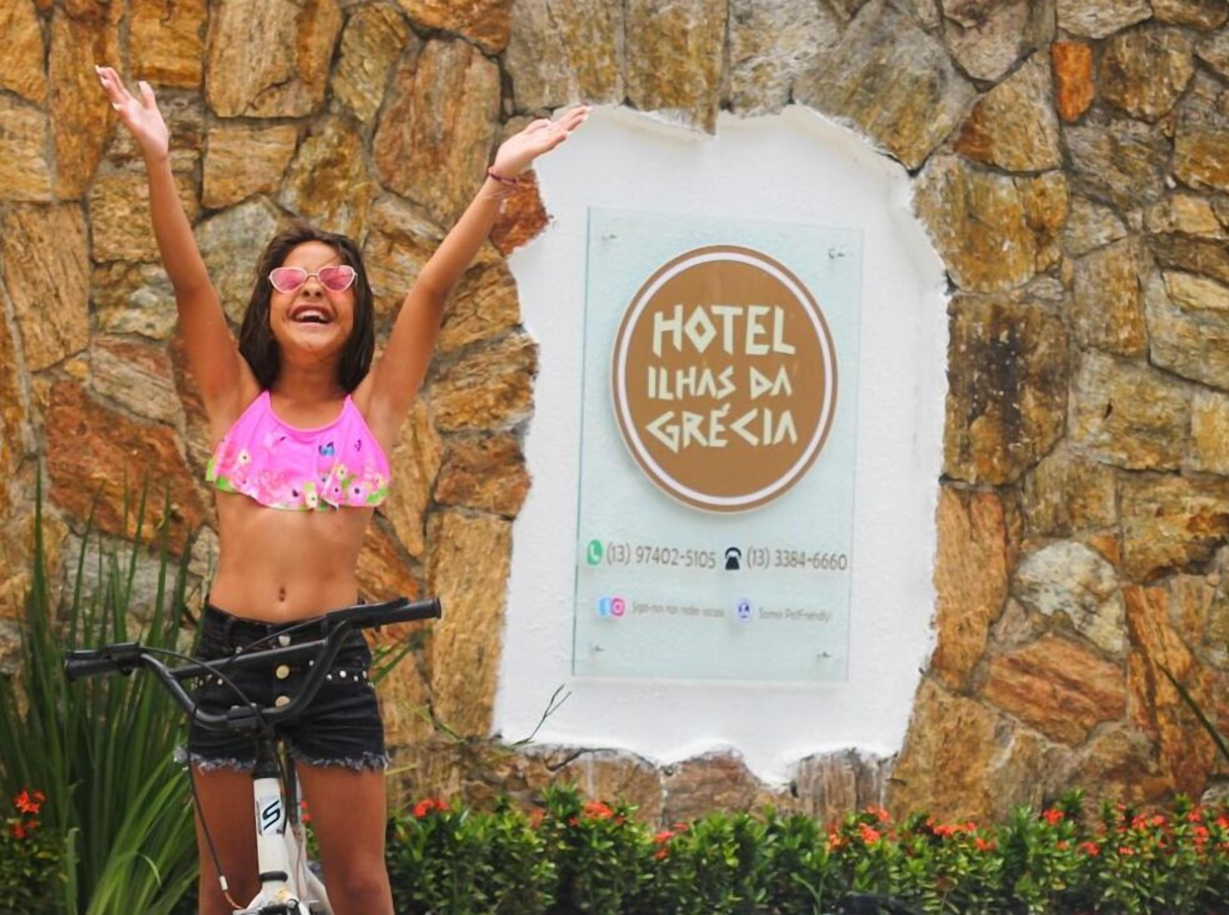 Eine Person steht vor einem Schild für HOTEL ILHAS DA GRÉCIA, im Hintergrund eine Steinmauer.