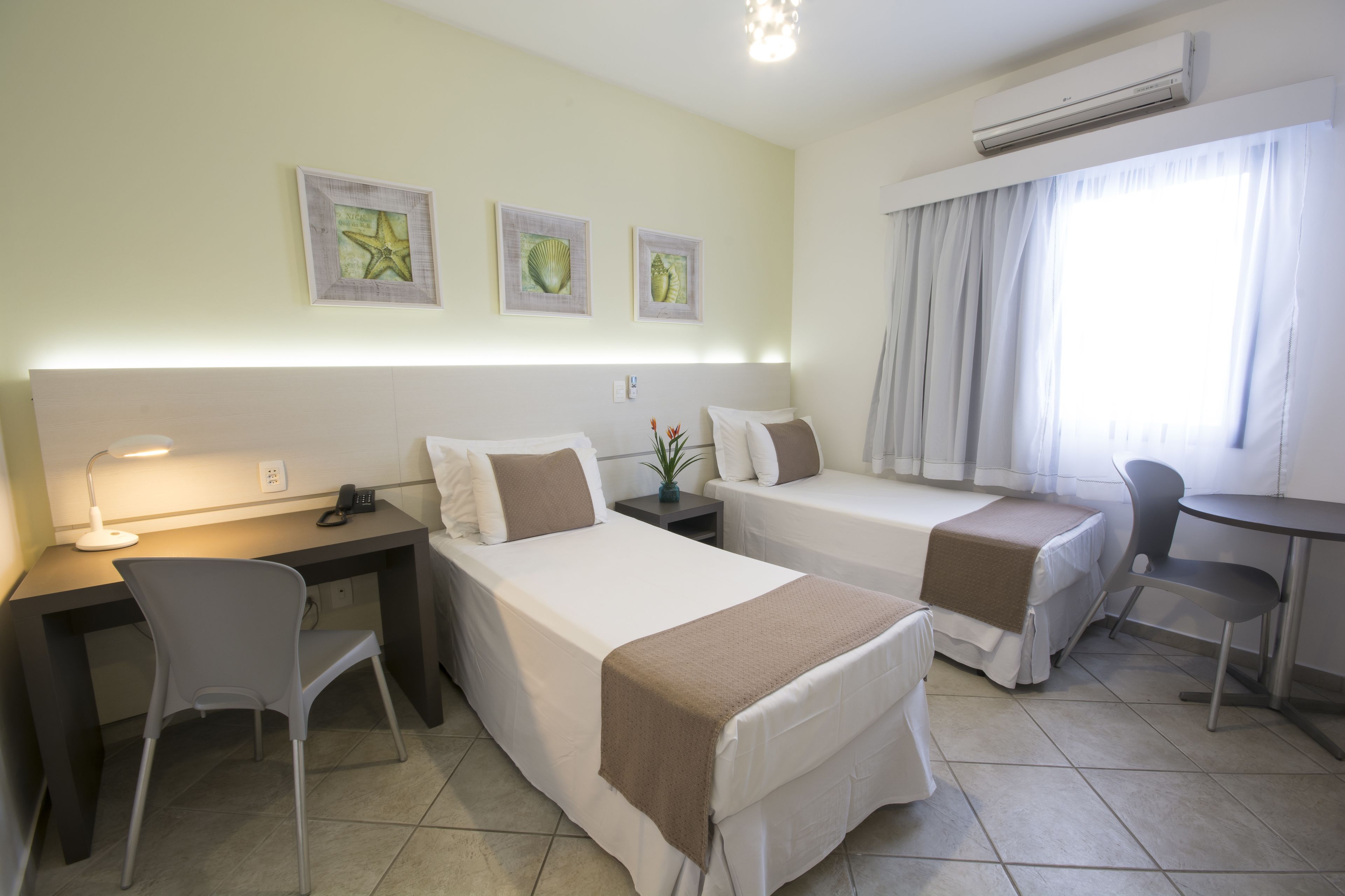 A hotel room with two beds, a desk, a chair, a small table, and a window with curtains.