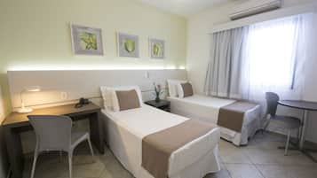A hotel room with two beds, a desk, a chair, a small table, and a window with curtains.