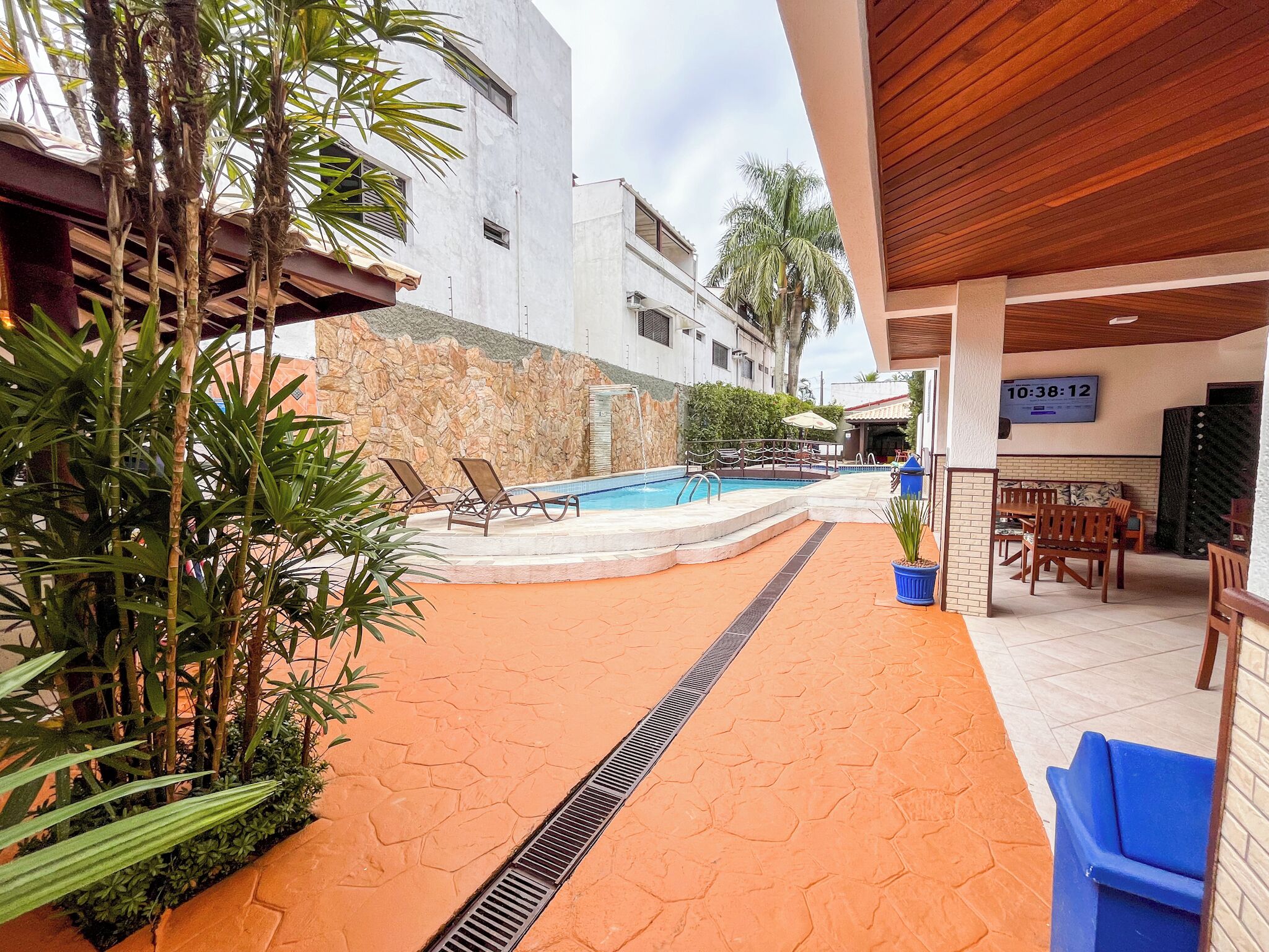 Un área de piscina con sillas de descanso, un muro de piedra y una zona de estar cubierta con un reloj.