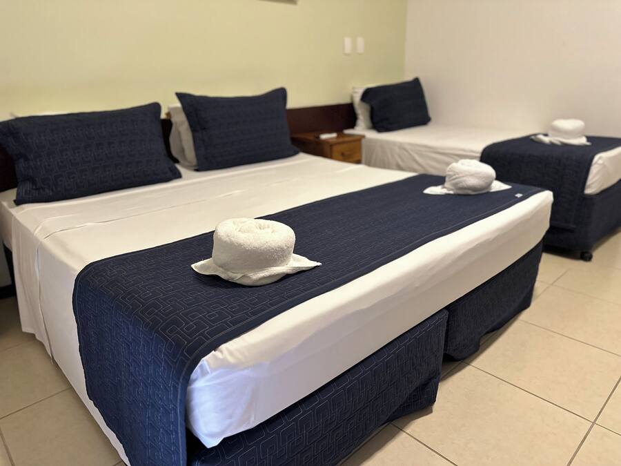 A hotel room with two beds, each with a white pillow and a blue headboard.