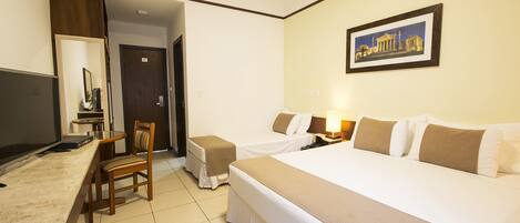 A hotel room with a large bed, a desk with a chair, a small table, and a framed picture on the wall.