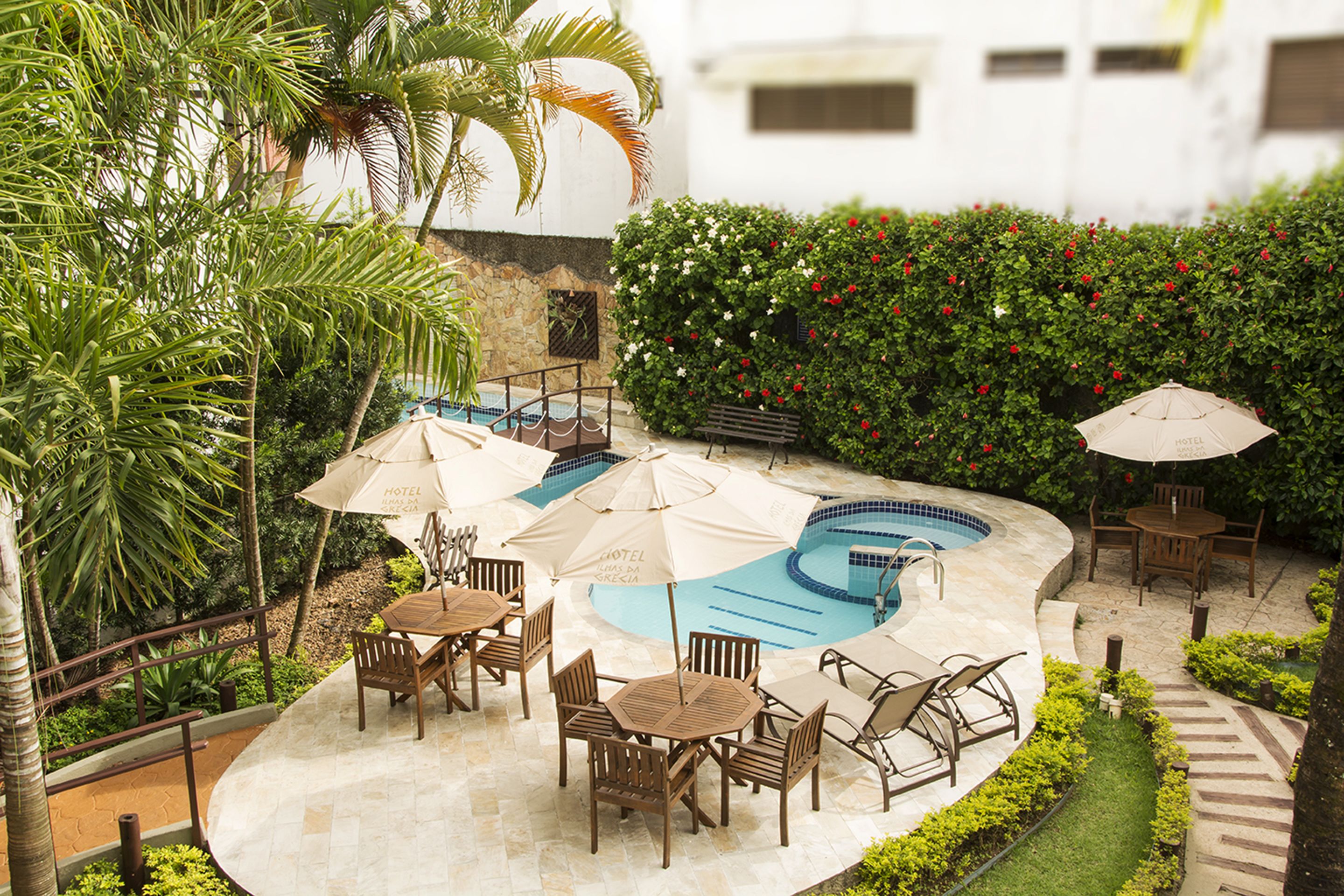 A pool area with multiple lounge chairs and umbrellas, surrounded by lush greenery and a stone wall.