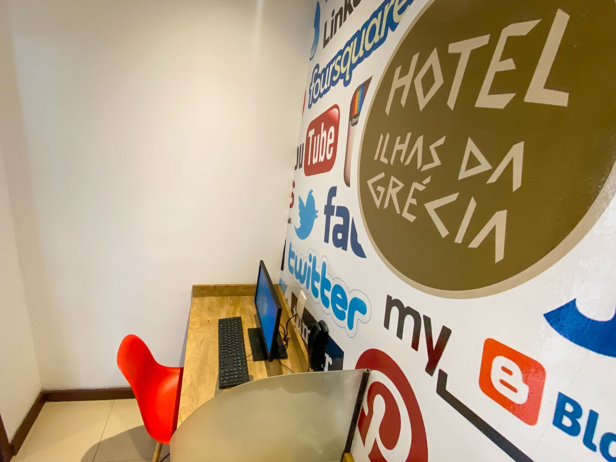 Una habitación con un escritorio, una silla roja y una pared decorada con varios logotipos de redes sociales.