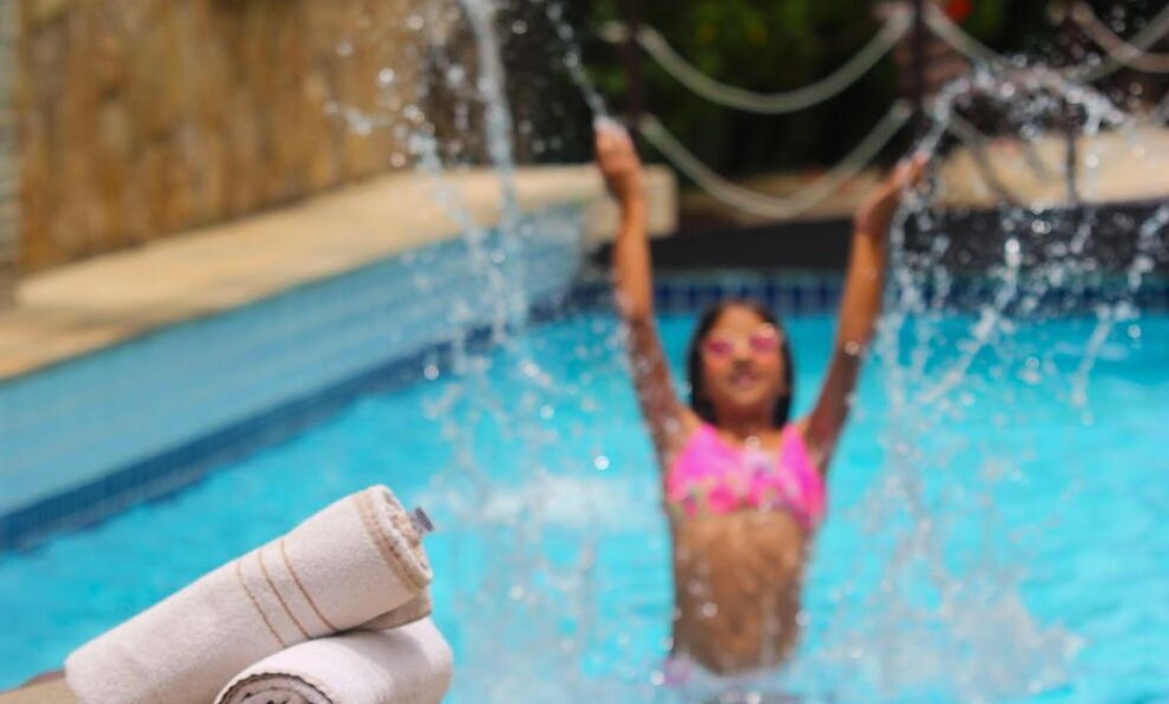 A person in a pink swimsuit in a swimming pool with water spraying upwards.