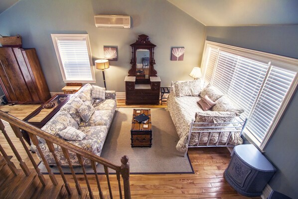 A cozy living room with a wooden staircase, a sofa, a bed, a dresser, and a mirror.