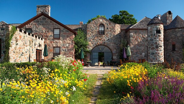 A stone building with a central archway, surrounded by colorful flower beds and a paved walkway. - Ste. Anne's Spa (Alnwick/Haldimand)