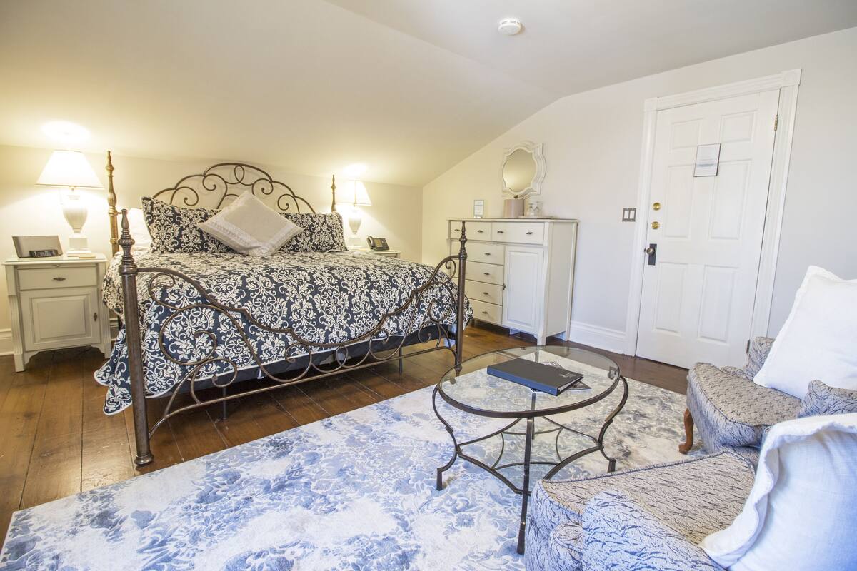 Un dormitorio con cama, mesitas de noche, cómoda, silla y una pequeña mesa redonda.