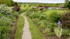 A garden pathway leading to a rustic building with a pool and umbrellas. - Ste. Anne's Spa (Alnwick/Haldimand)