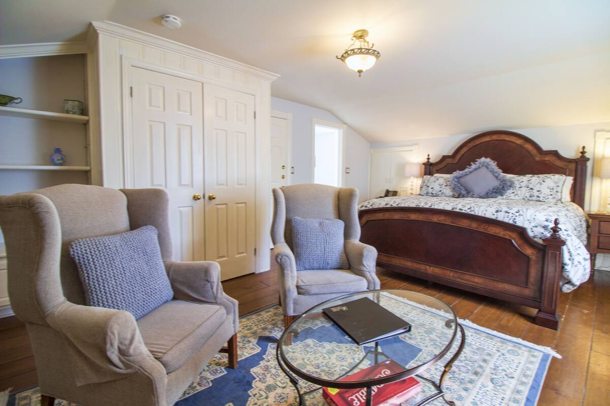Un dormitorio con una cama grande, dos sillones, una mesita y un armario.