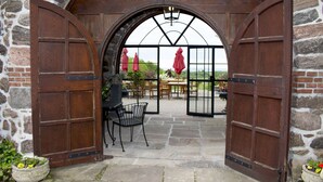 An arched stone doorway leading to an outdoor patio with stone flooring, a table, chairs, and potted plants. - Ste. Anne's Spa (Alnwick/Haldimand)
