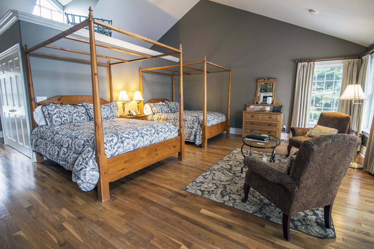 Un dormitorio amplio con cama con dosel, dos camas más pequeñas, un aparador de madera, una silla y un ventanal grande.