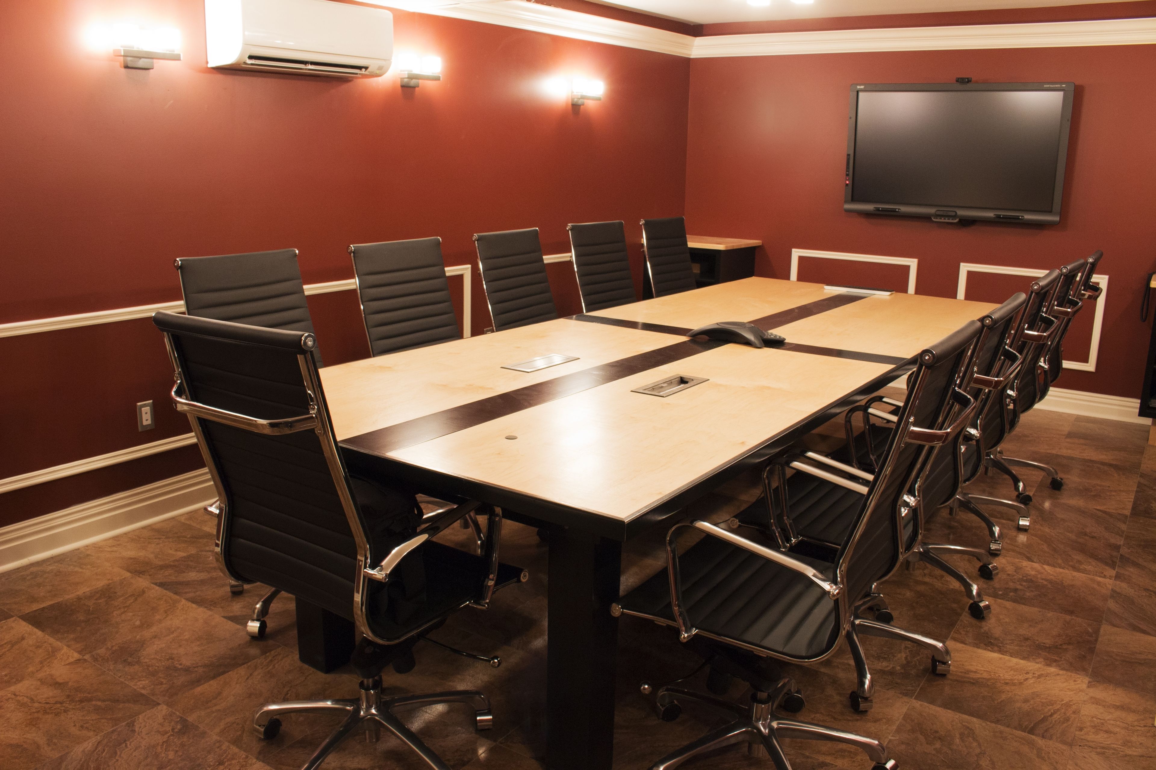 A conference room with a long table, black chairs, and a flat-screen TV on the wall.