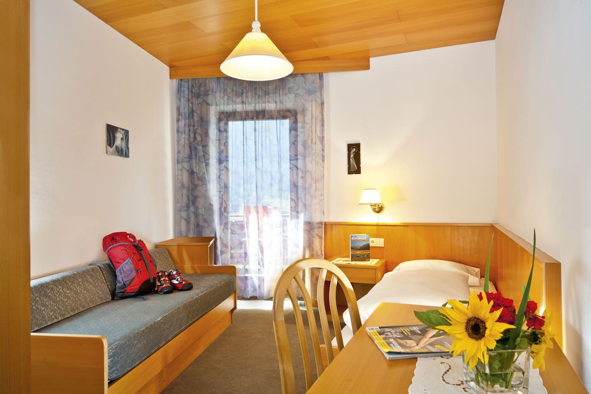 A hotel room with a wooden ceiling, a sofa, a dining table with a vase of flowers, and a bed with a nightstand.