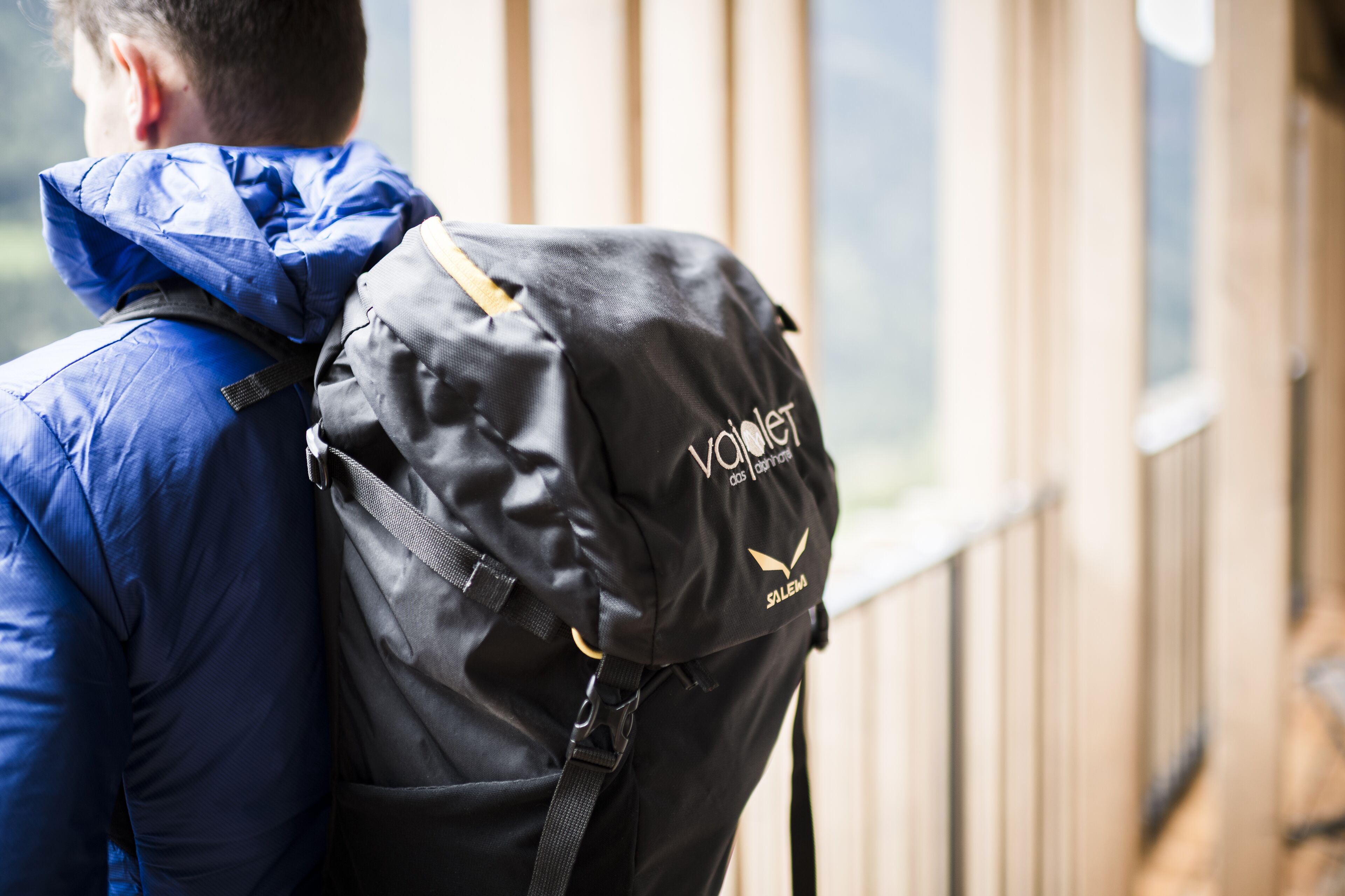 A person wearing a blue jacket with a black bag on their back.