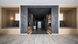 Un couloir moderne aux murs en bois et doté de bancs, qui mène à une pièce lumineuse avec une grande fenêtre.