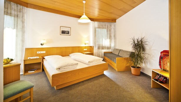 Une chambre à coucher avec un lit en bois, des tables de chevet, un banc, une plante en pot et un sac rouge.