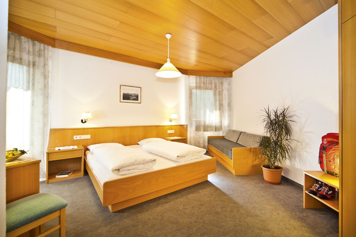 A bedroom with a wooden bed, bedside tables, a bench, a potted plant, and a red bag.