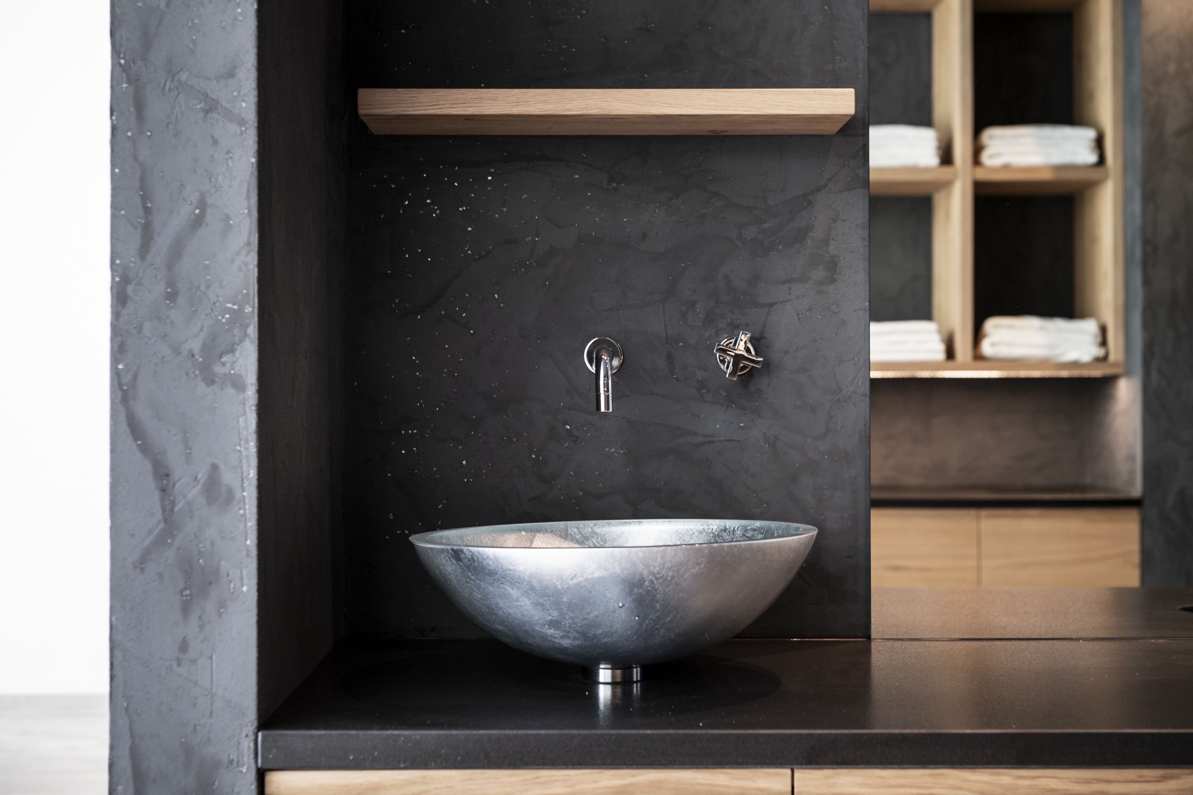 A modern bathroom with a large, round, metallic sink centered on a dark countertop.