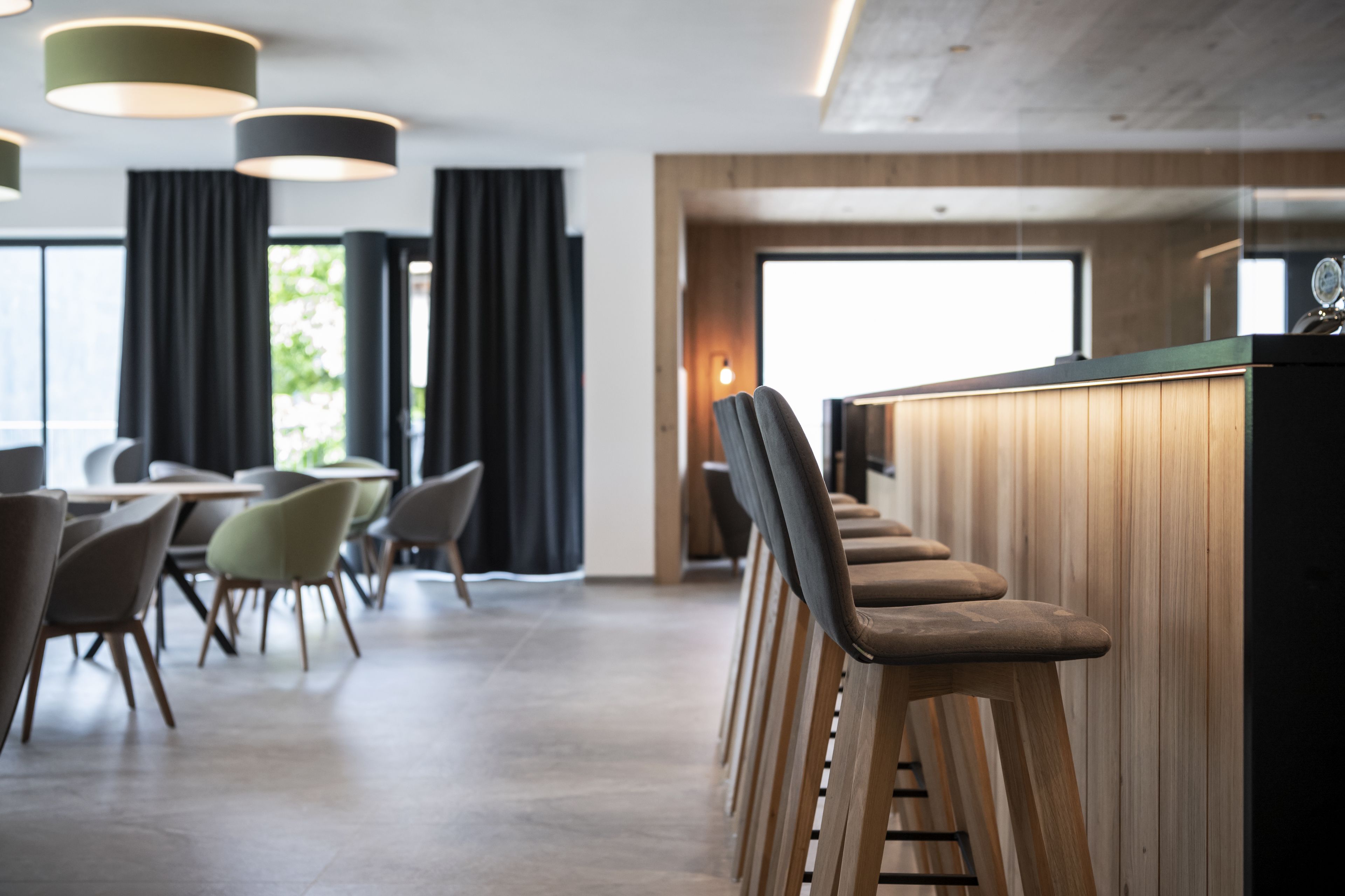 A modern bar area with wooden stools and a counter, surrounded by dining tables and chairs.