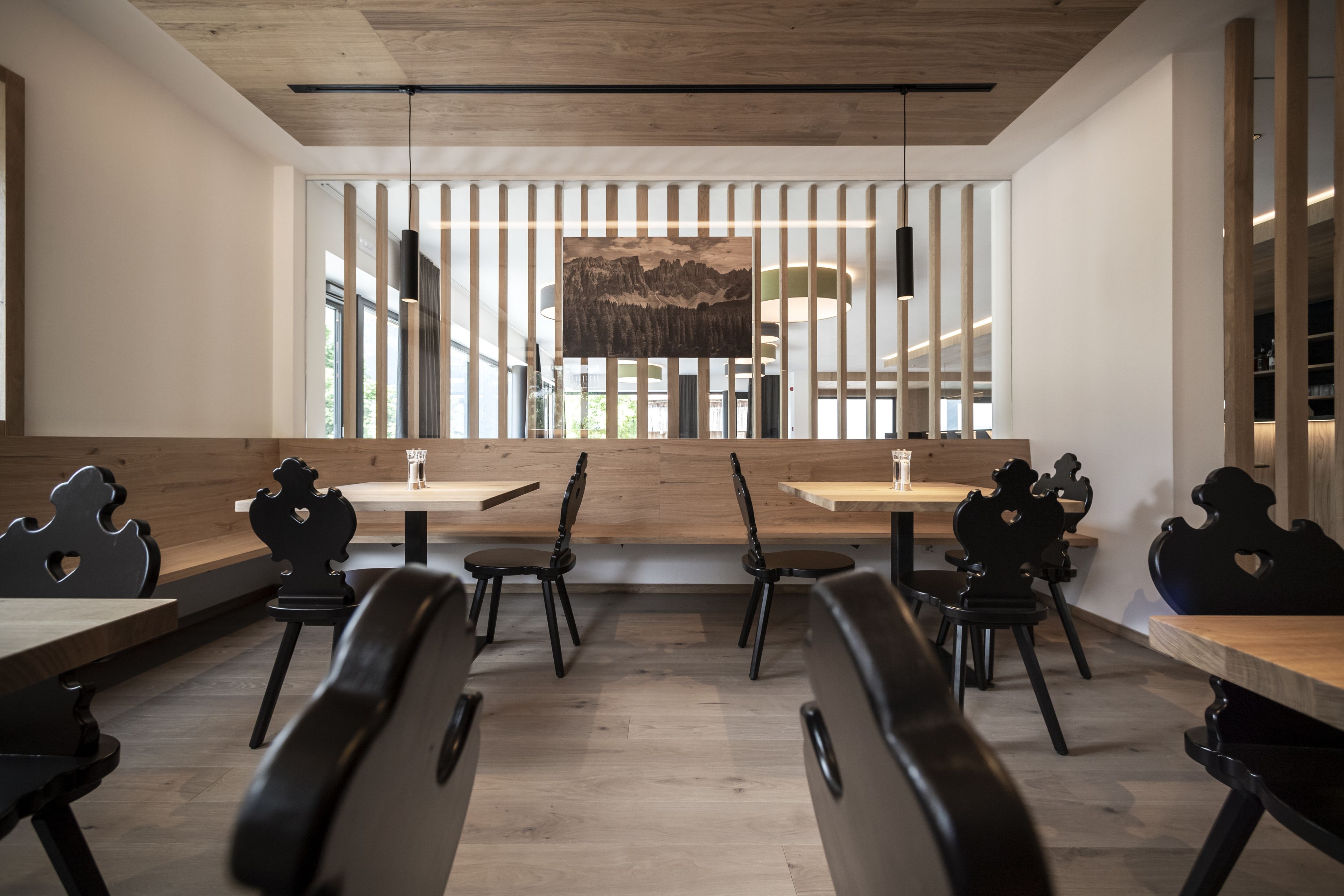 Un comedor moderno con mesas de madera y sillas negras, un cuadro grande en la pared y vistas al exterior.