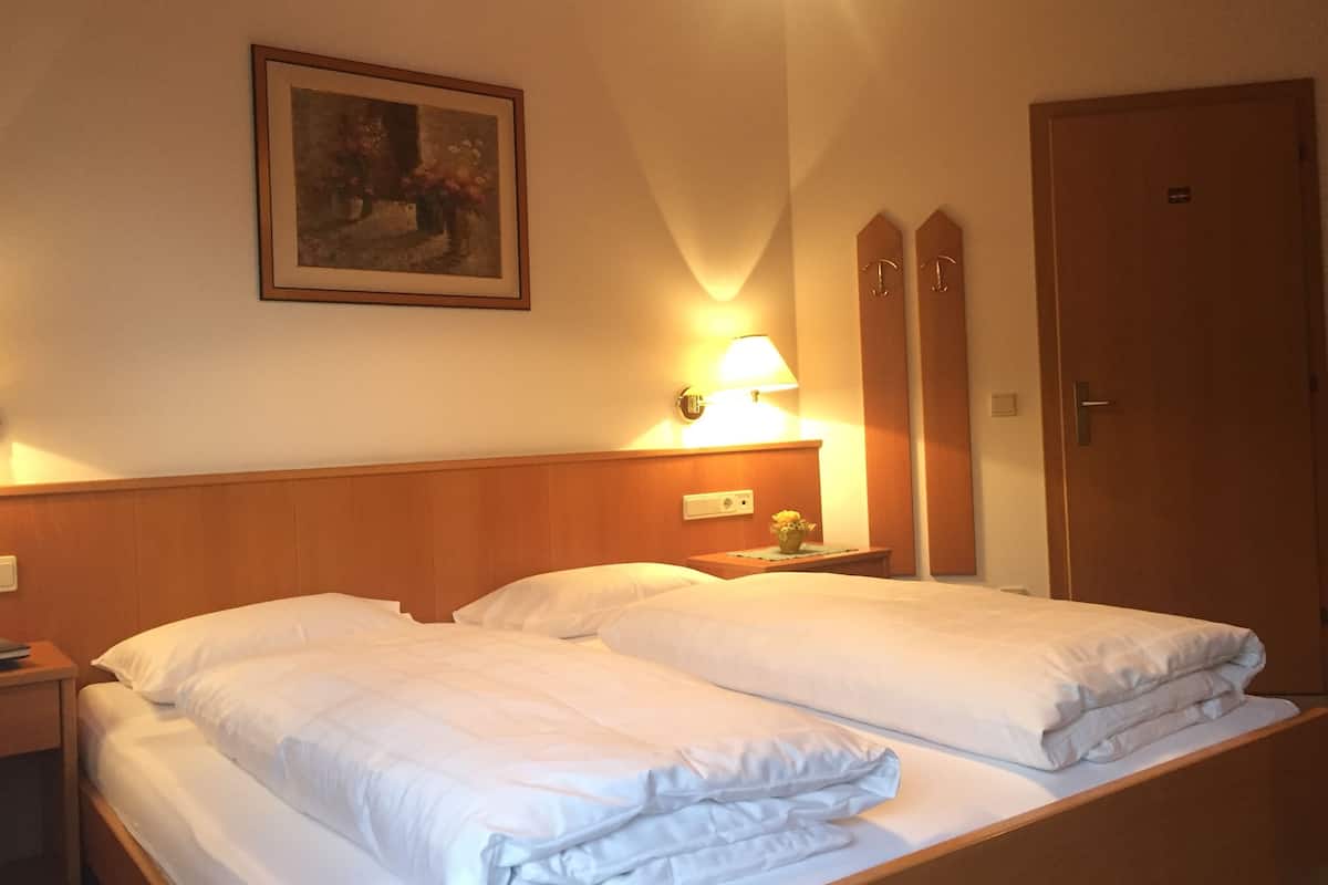A hotel room with two beds, a nightstand with a lamp, a framed picture on the wall, and a wooden wardrobe.