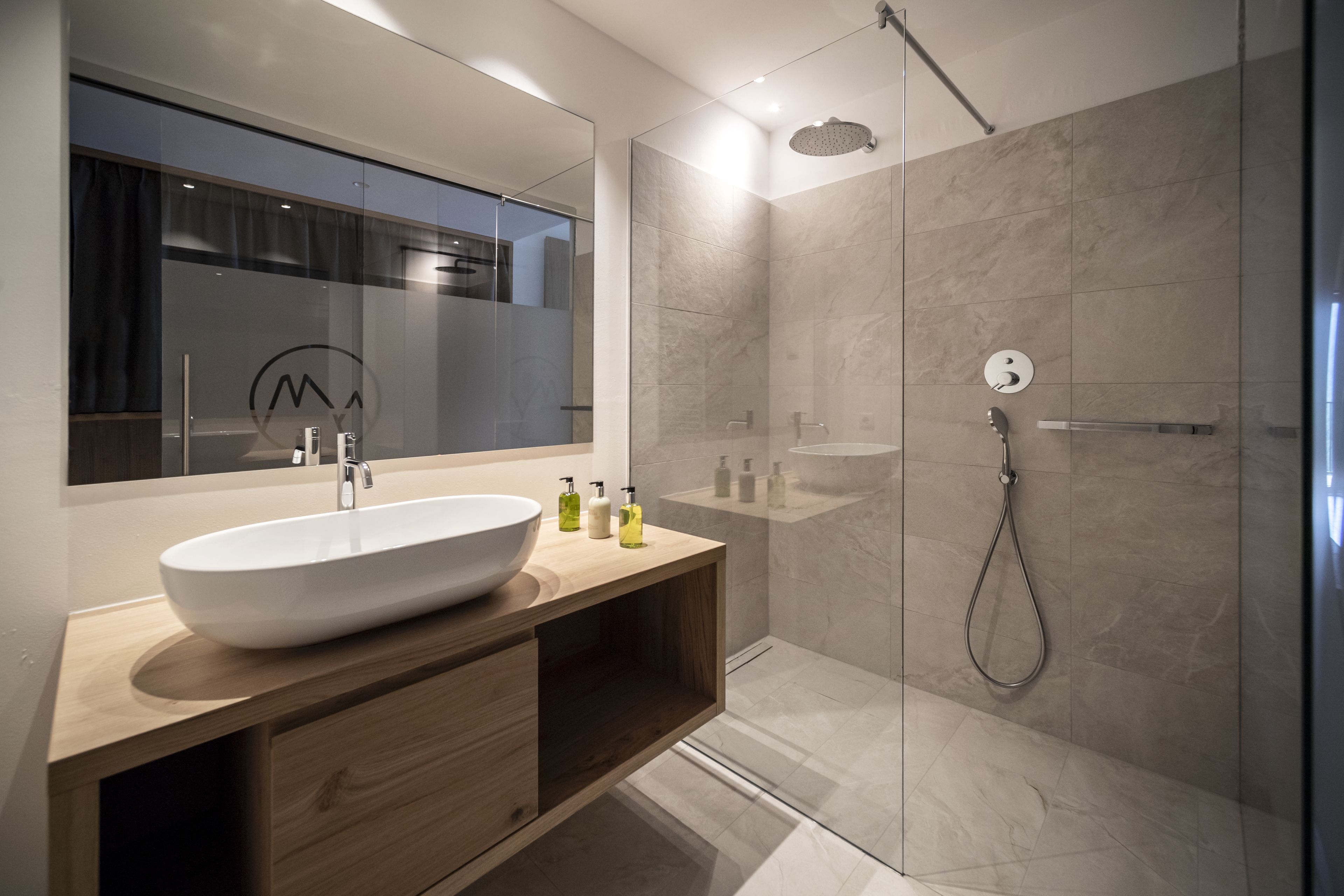 Un baño moderno con un lavamanos de diseño, tocador de madera y zona de ducha con mampara de vidrio.