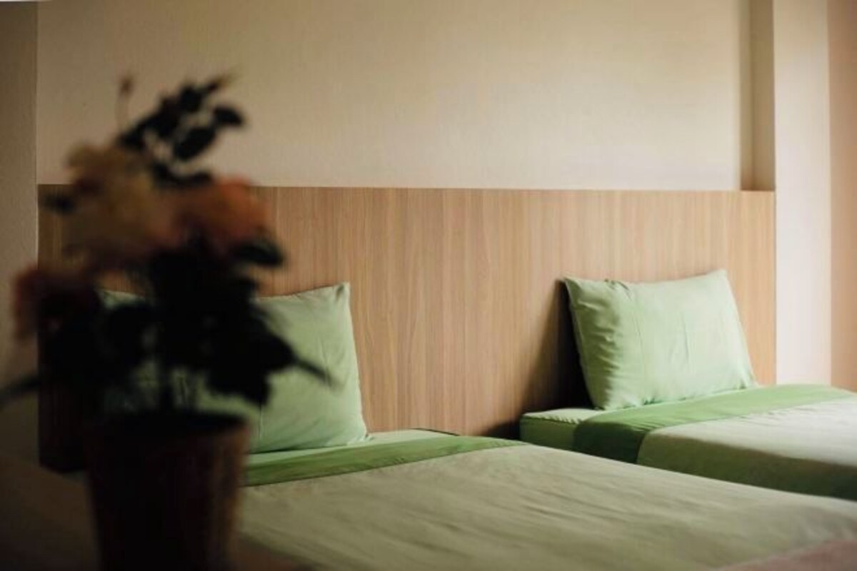 A hotel room with two beds, each with a green bedspread and matching pillows.