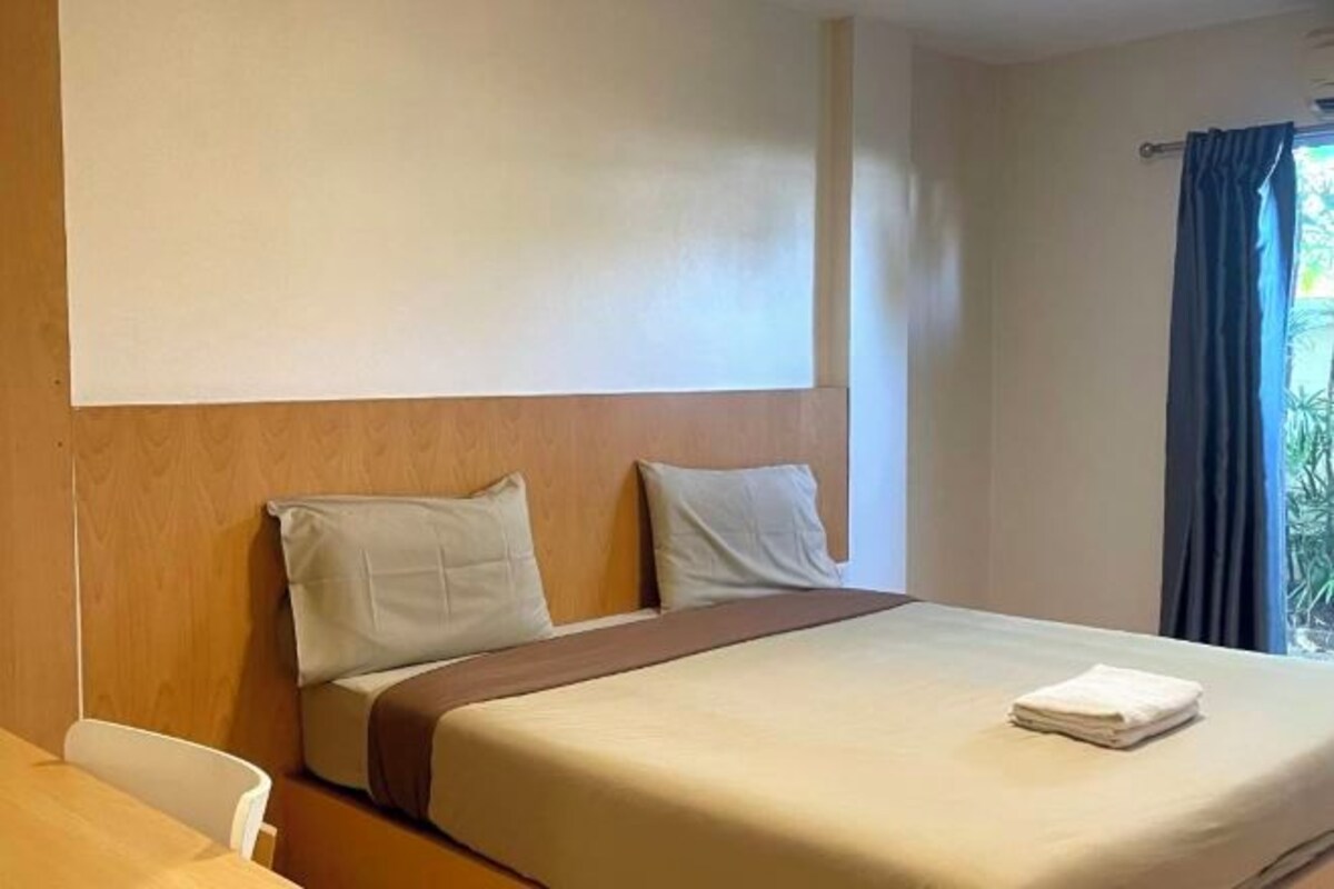 Une chambre d’hôtel avec un lit, une tête de lit en bois, une fenêtre avec des rideaux et une vue sur la verdure.