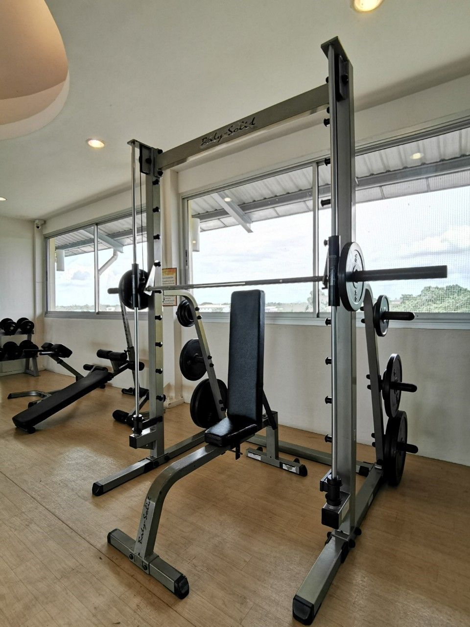 Un gimnasio con equipo de levantamiento de pesas, incluyendo una jaula para sentadillas y bancos.